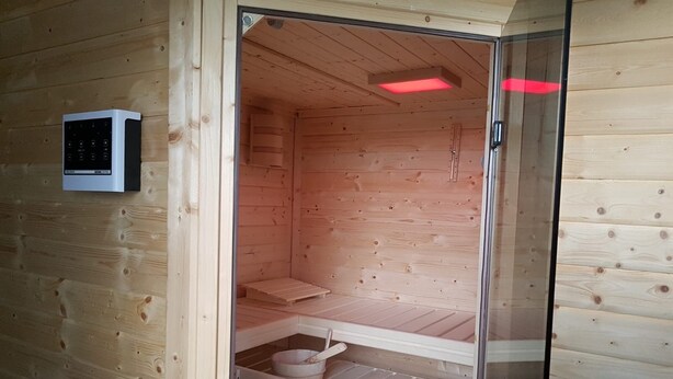 A wooden sauna with a glass door, a control panel, and a bench. - With us (Tittling)