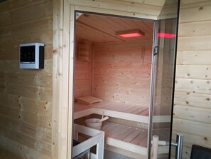 Un sauna en bois doté d’une porte en verre, d’un panneau de commande et d’un banc.