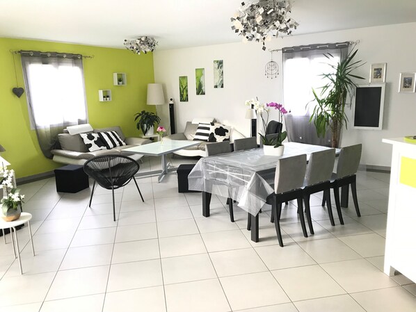 A modern living room with a dining area, green walls, and a chandelier.