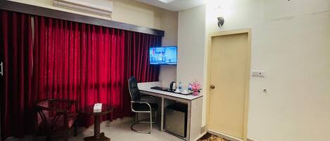 A hotel room with a desk, chair, and a television mounted on the wall.