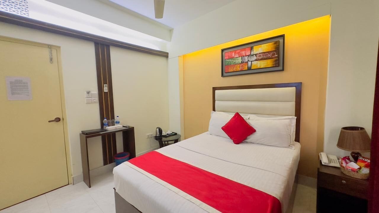 A hotel room with a bed, a bedside table, a lamp, and a wall-mounted painting.