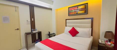 A hotel room with a bed, a bedside table, a lamp, and a wall-mounted painting.