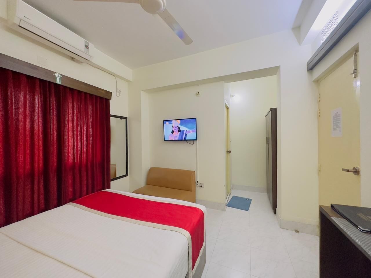 A hotel room with two beds, a television, a ceiling fan, and a door leading to a corridor.