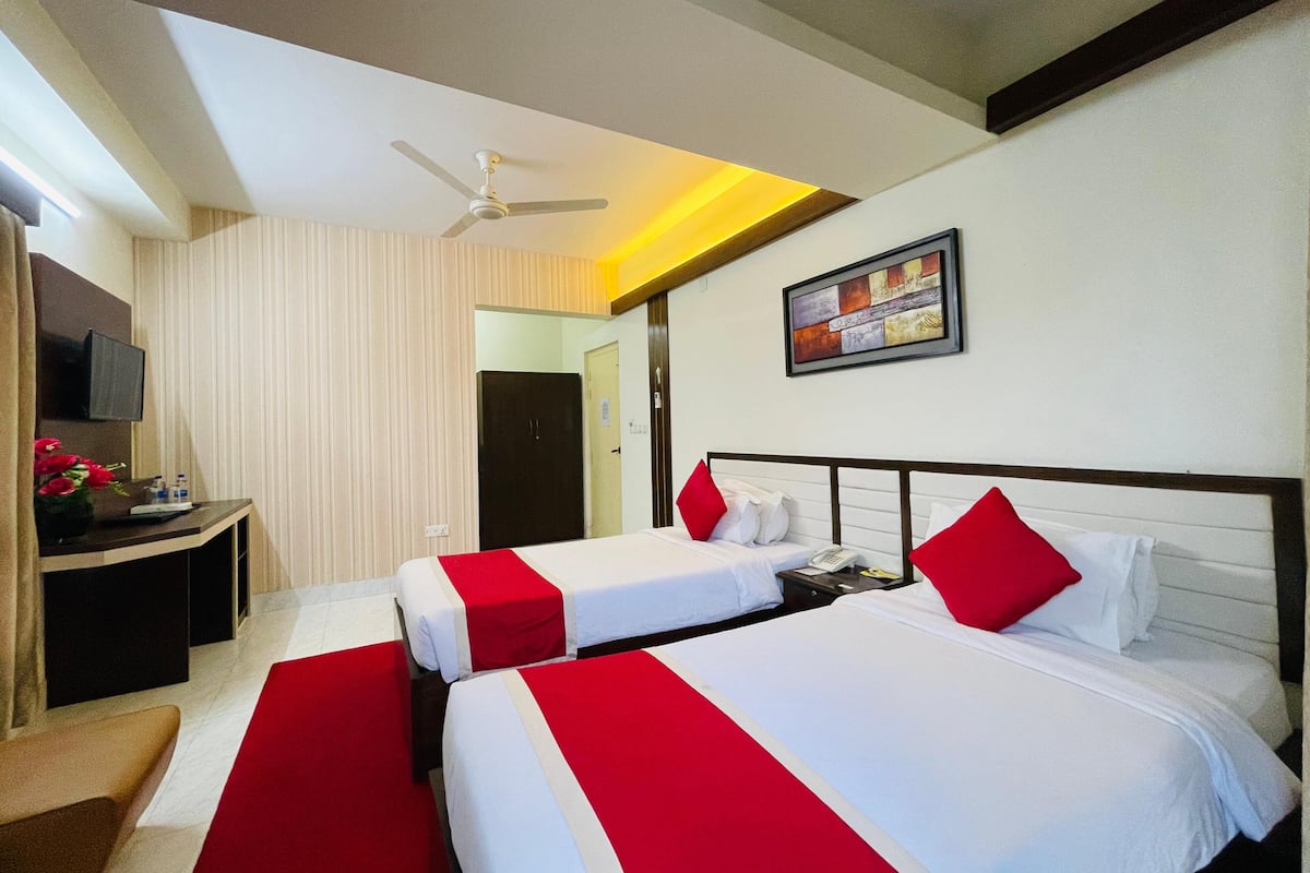 A hotel room with two beds, a desk, a TV, and a ceiling fan.