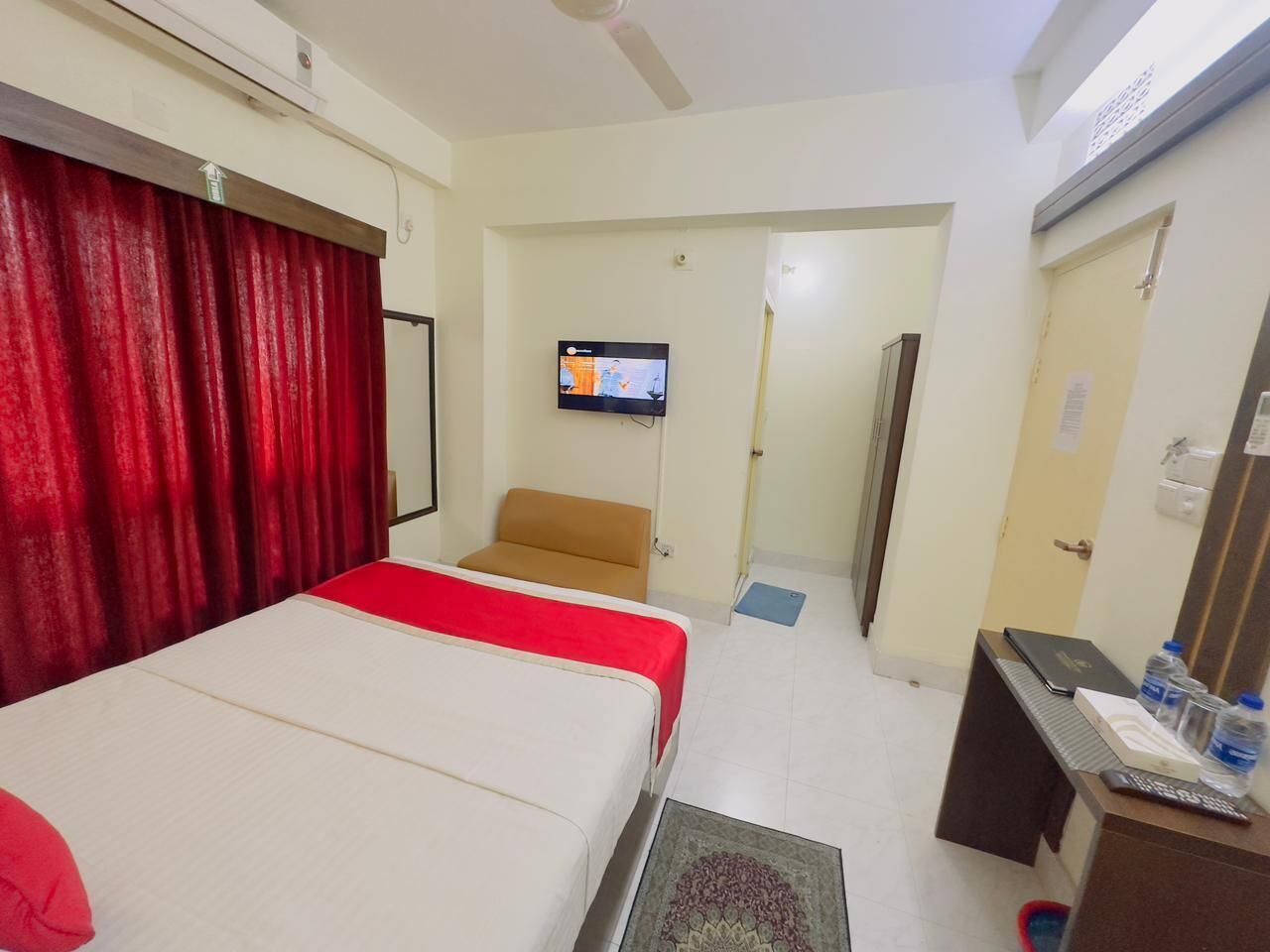 A hotel room with two beds, a television, a desk with a laptop, and a door leading to another room.