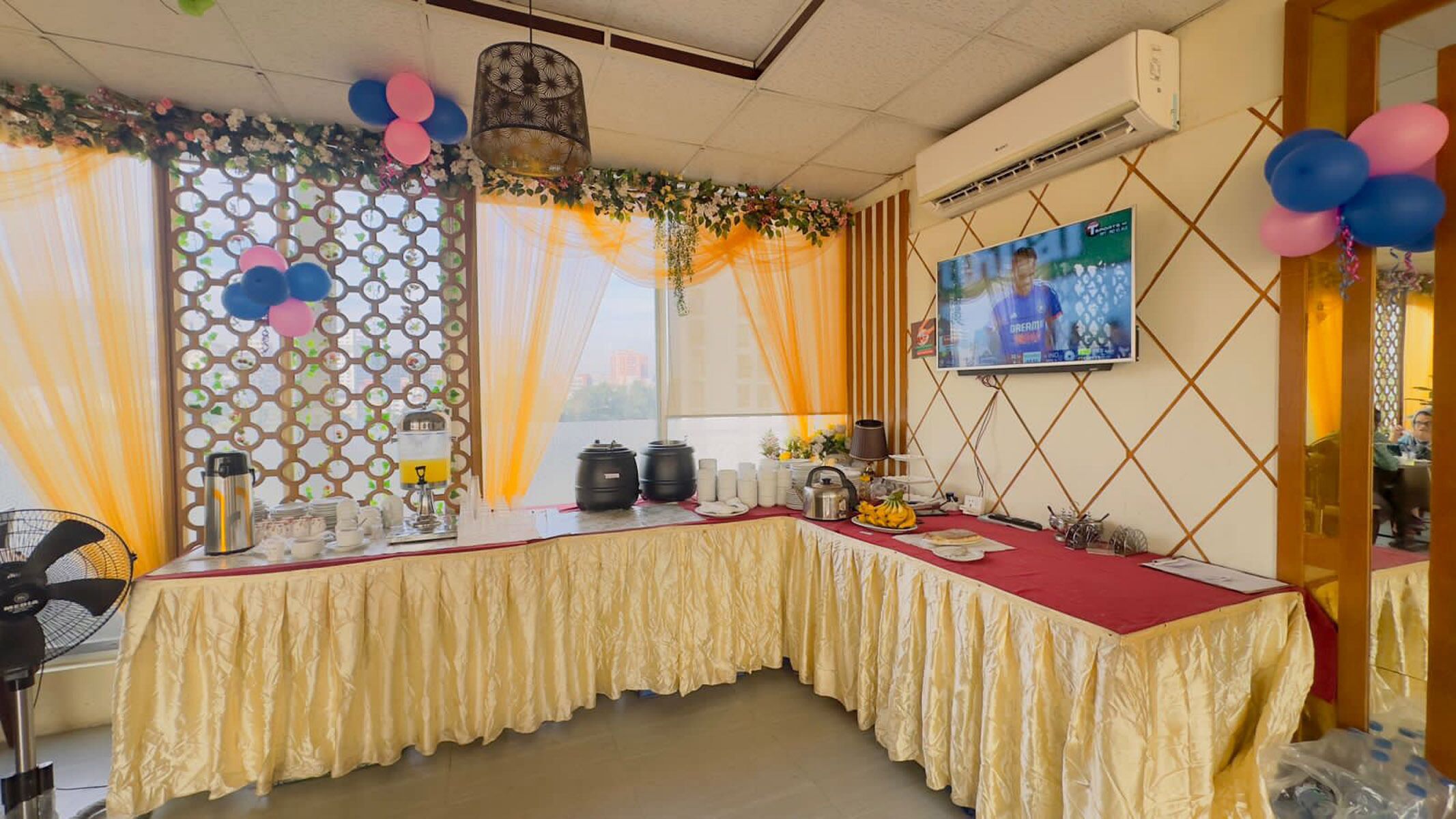 A conference room with a table set for a meeting, a television screen, and decorative elements like balloons and drapes.