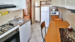 A compact kitchen with a gas stove, sink, white cabinets, a refrigerator, and a microwave. - Residence Parco Ducale (Parma)