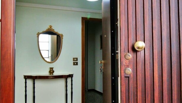 A hallway with a wooden door, a mirror, a small table, and a ceiling light. - Residence Parco Ducale (Parma)