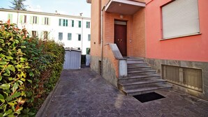 A narrow stone pathway leading to a building with a red facade, a wooden door, and a small set of stairs. - Residence Parco Ducale (Parma)