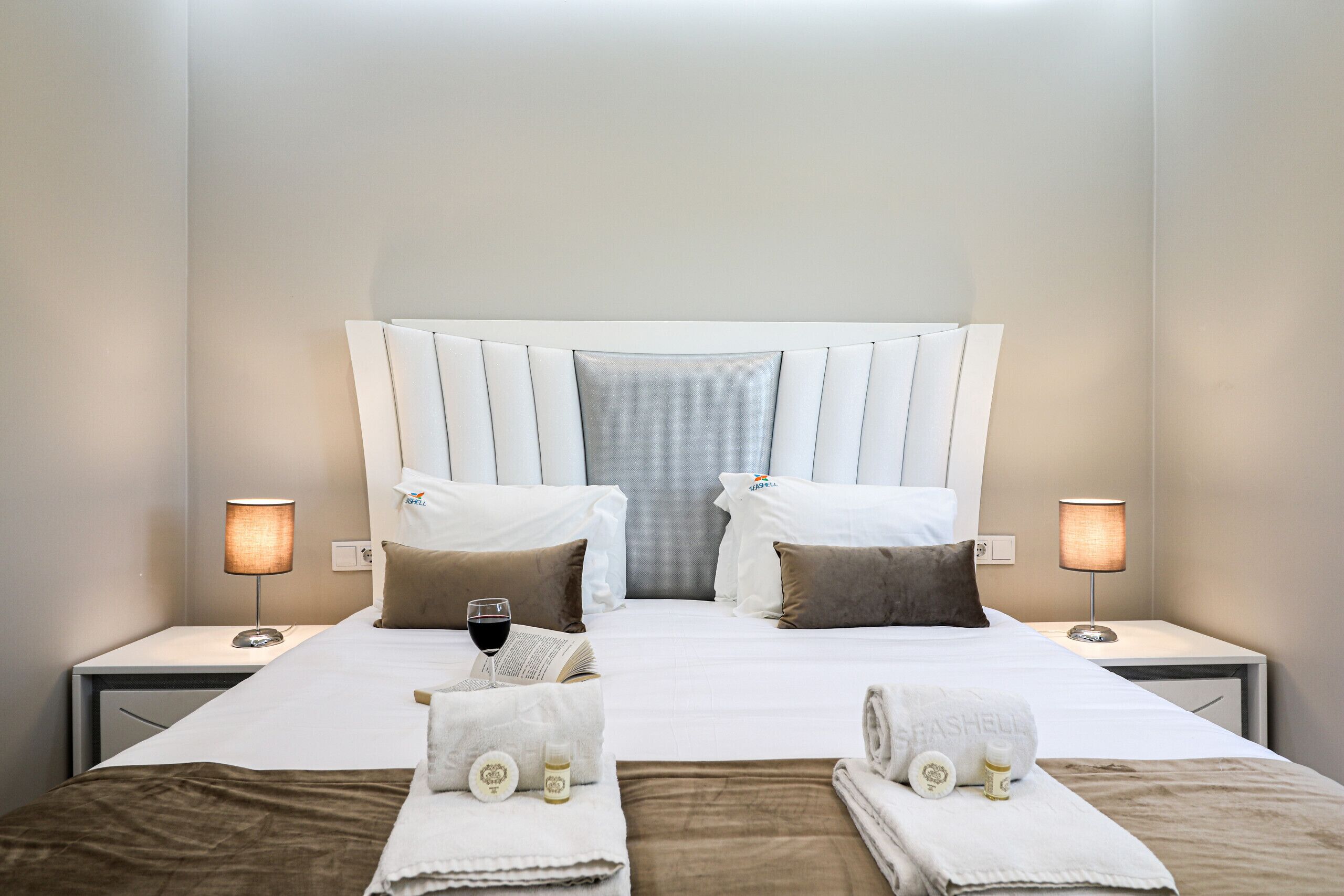 A neatly made bed with pillows, a bedside table with a lamp, and a glass of wine on the nightstand.