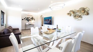 Una sala de estar moderna con una mesa de comedor de vidrio, sillas blancas, un sofá marrón y arte decorativo en la pared.