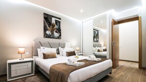 Una habitación de hotel moderna con una cama grande, una mesita de noche con lámpara, un espejo y una puerta.