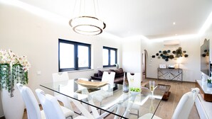 Un comedor moderno con una mesa de vidrio, sillas blancas y un sofá al fondo.