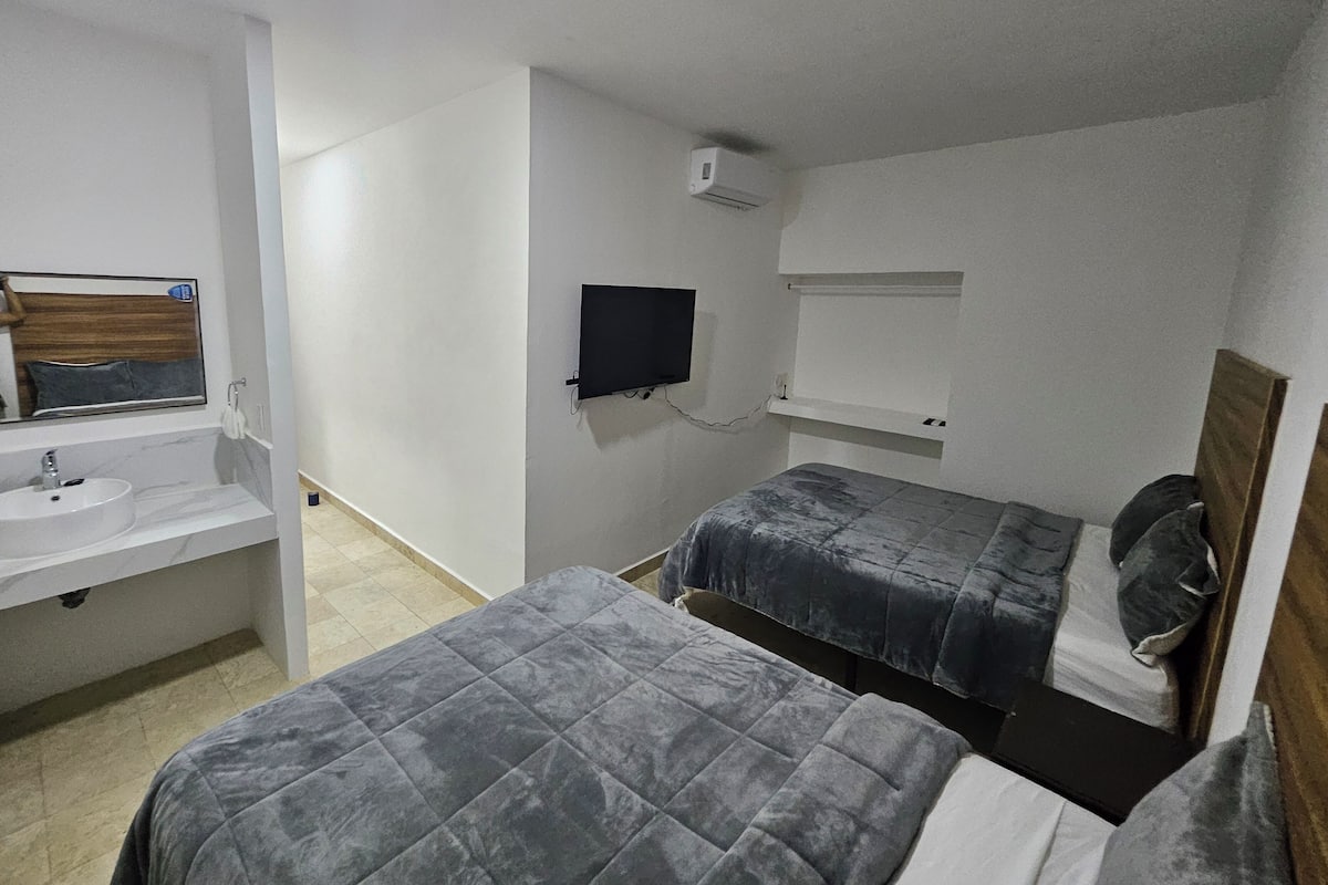 Una habitación pequeña y limpia con una cama, una mesita de noche, un espejo y un televisor montado en la pared.