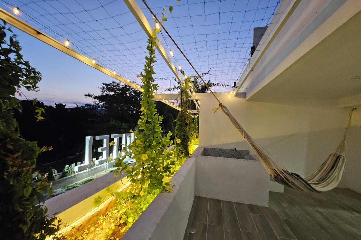 Un balcón con hamaca, plantas e iluminación colgante.