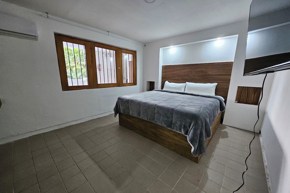 Un dormitorio con cama, una ventana con rejas, cabecera de madera y suelo de baldosas.