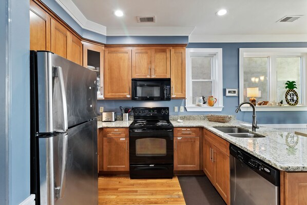 A modern kitchen with wooden cabinets, stainless steel appliances, granite countertops, and a window with a view.