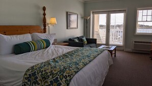 A hotel room with a large bed, a sofa, a desk, and a view of the city through the windows. - Inlet Inn NC (Beaufort)