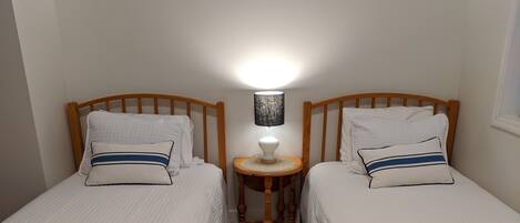 A twin bedroom with two single beds, a bedside table with a lamp, and a patterned rug.