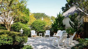 A patio with white Adirondack chairs and a table, surrounded by lush greenery and a white fence. - Inlet Inn NC (Beaufort)