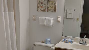 A bathroom with a toilet, sink, and shower curtain. There are two framed pictures on the wall and a towel rack with towels.