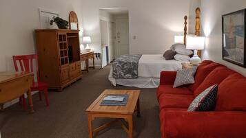 Une pièce comprenant un lit, un canapé rouge, une table en bois, une chaise rouge, un meuble en bois et une lampe.