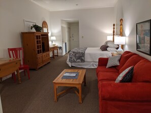 A room with a bed, a red sofa, a wooden table, a red chair, a wooden cabinet, and a lamp.