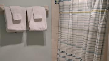 Kylpyhuone, jossa on suihkuverho, kaksi pyyhettä, wc-istuin, roskakori ja wc-paperiteline.
