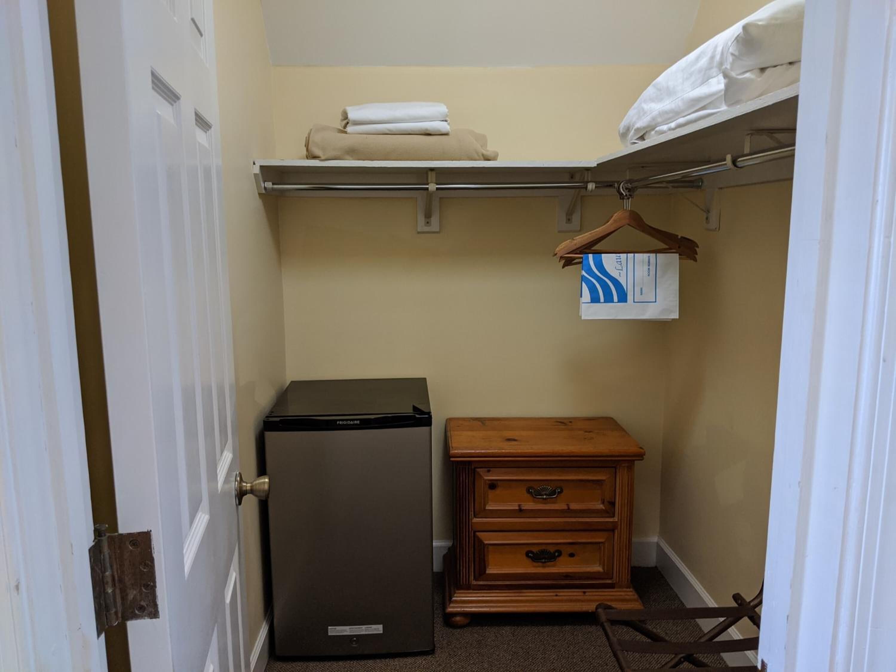 Une petite pièce comprenant un réfrigérateur, une commode en bois et une étagère avec des serviettes pliées.