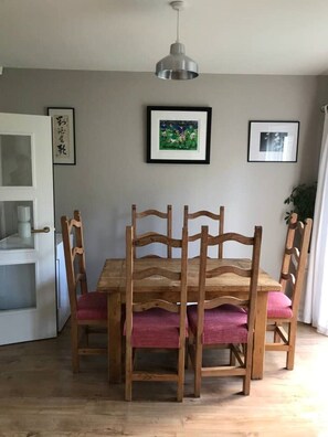 A dining area with a wooden table and chairs, a hanging pendant light, and framed artwork on the wall. - Townhouse on the coast (Portrush)