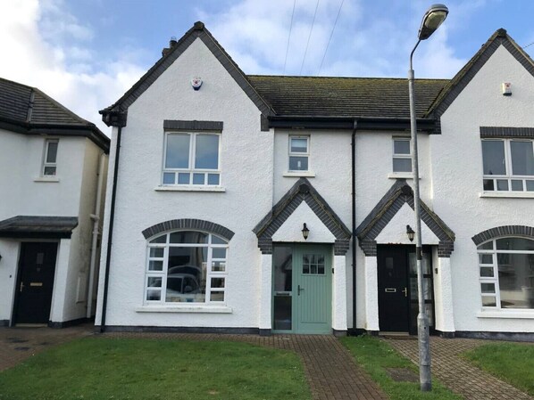 A row of white buildings with black roofs and green doors, featuring a symmetrical architectural design with arched windows and a central entrance. - Townhouse on the coast (Portrush)