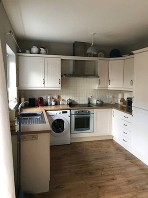 A compact kitchen with white cabinets, a washing machine, an oven, and a sink. - Townhouse on the coast (Portrush)