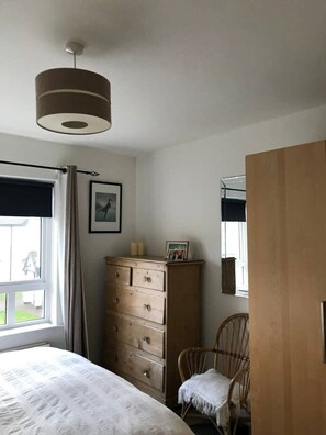 A bedroom with a bed, a dresser, a chair, a window with curtains, and a ceiling light. - Townhouse on the coast (Portrush)
