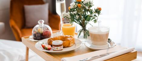 A breakfast tray with croissant, strawberries, jam, orange juice, coffee, and flowers on a bed.