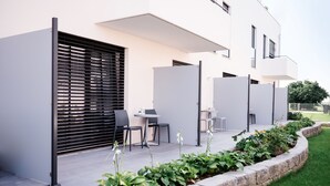 A modern outdoor seating area with a table and chairs, a planter with greenery, and a building with a white facade and black shutters. - HAIMHAUSERS Hotel Garni (Haimhausen)