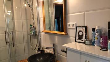 A modern bathroom with a glass-enclosed shower, a black vessel sink, and a white vanity with toiletries.