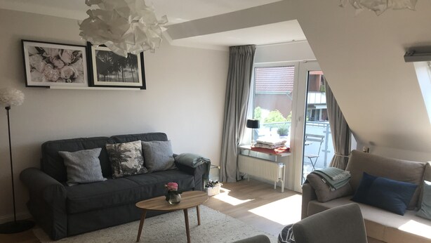 Un salon moderne avec un canapé gris foncé, une table basse et une vue sur l’extérieur grâce à une grande fenêtre.