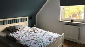 Une chambre à coucher avec un lit, une fenêtre donnant sur des arbres et un radiateur.