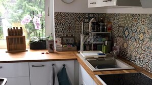 Une cuisine compacte avec des meubles blancs, un plan de travail en bois, un évier et une fenêtre donnant sur un espace verdoyant.