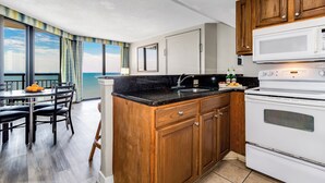 A kitchen with wooden cabinets, a black countertop, and a white stove. - 17th Floor 1Br Oceanfront/ Dogs OK! (Myrtle Beach)