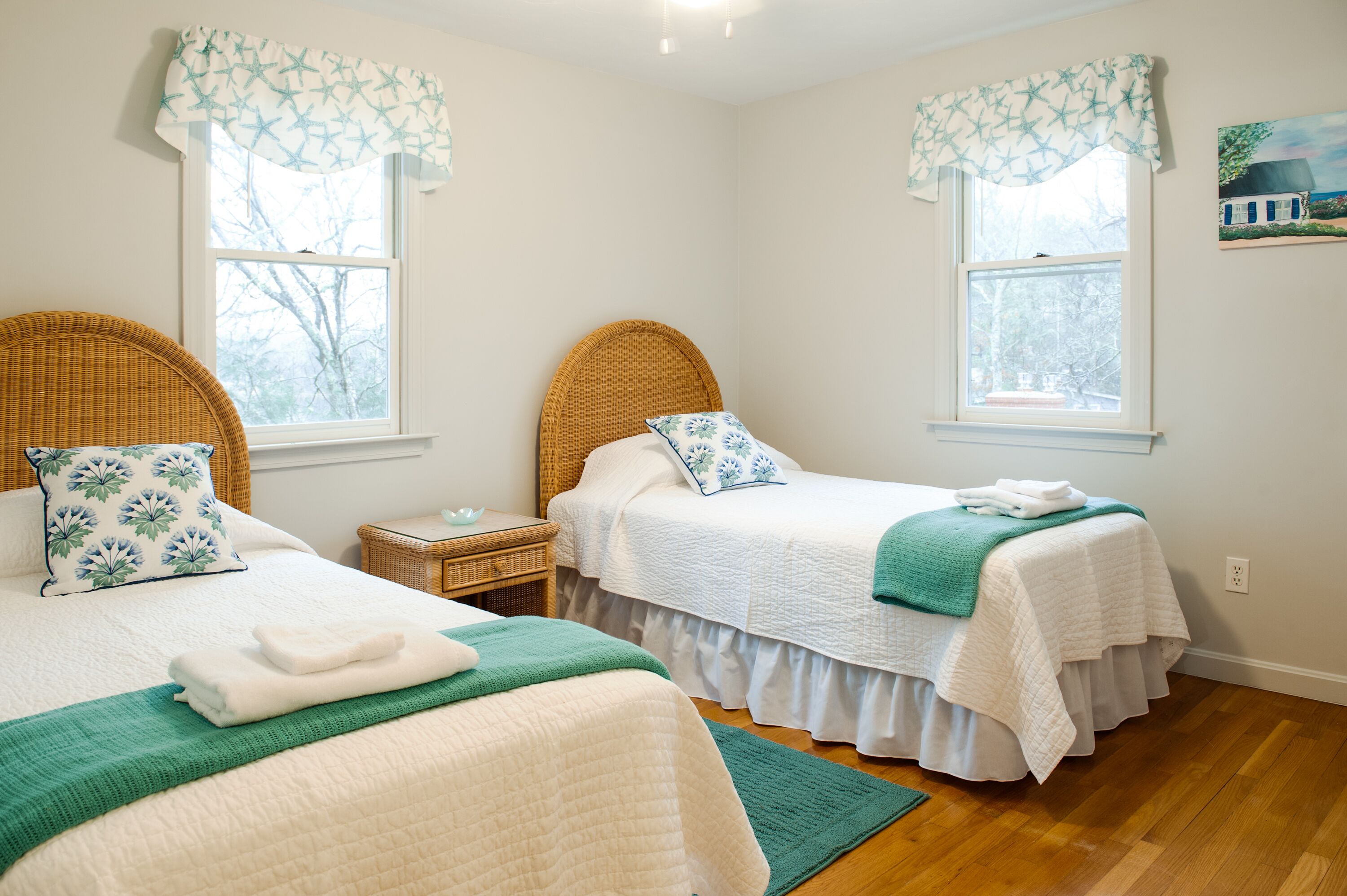 A bedroom with two beds, each with a headboard, a bedside table, and a window with a view of trees.