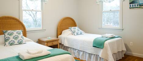 A bedroom with two beds, each with a headboard, a bedside table, and a window with a view of trees.