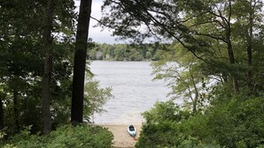 A pathway leading to a lake with a kayak docked on the shore, surrounded by dense foliage and trees. - Stunning 4-bedroom Private Fresh Water Beach Front (East Falmouth)