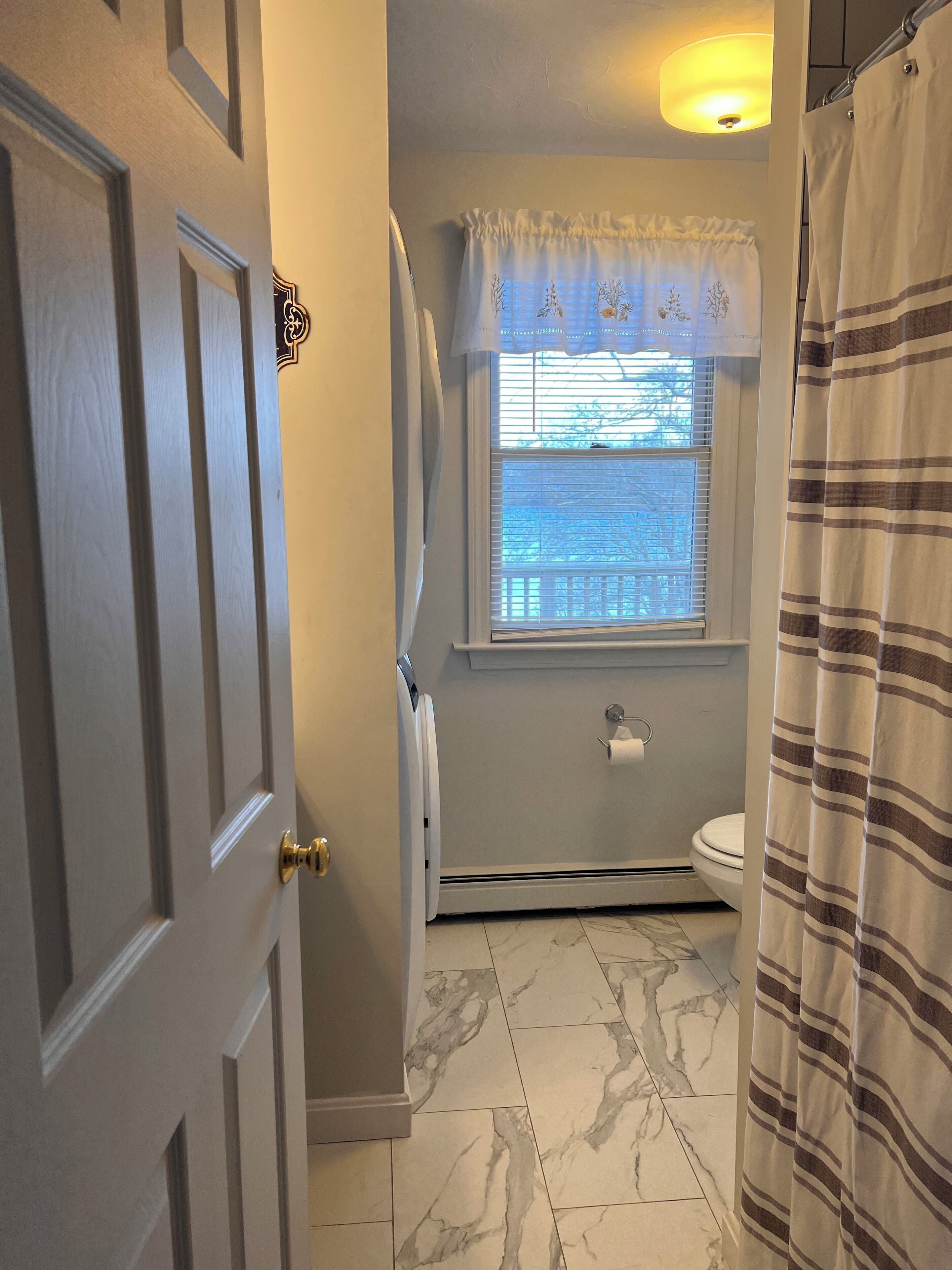 Une salle de bain avec des toilettes, une fenêtre avec un rideau et un rideau de douche.