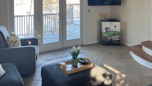 A living room with a wooden ceiling, a large TV, a sofa, a coffee table with a tray, and a sliding glass door leading to an outdoor deck. - Stunning 4-bedroom Private Fresh Water Beach Front (East Falmouth)