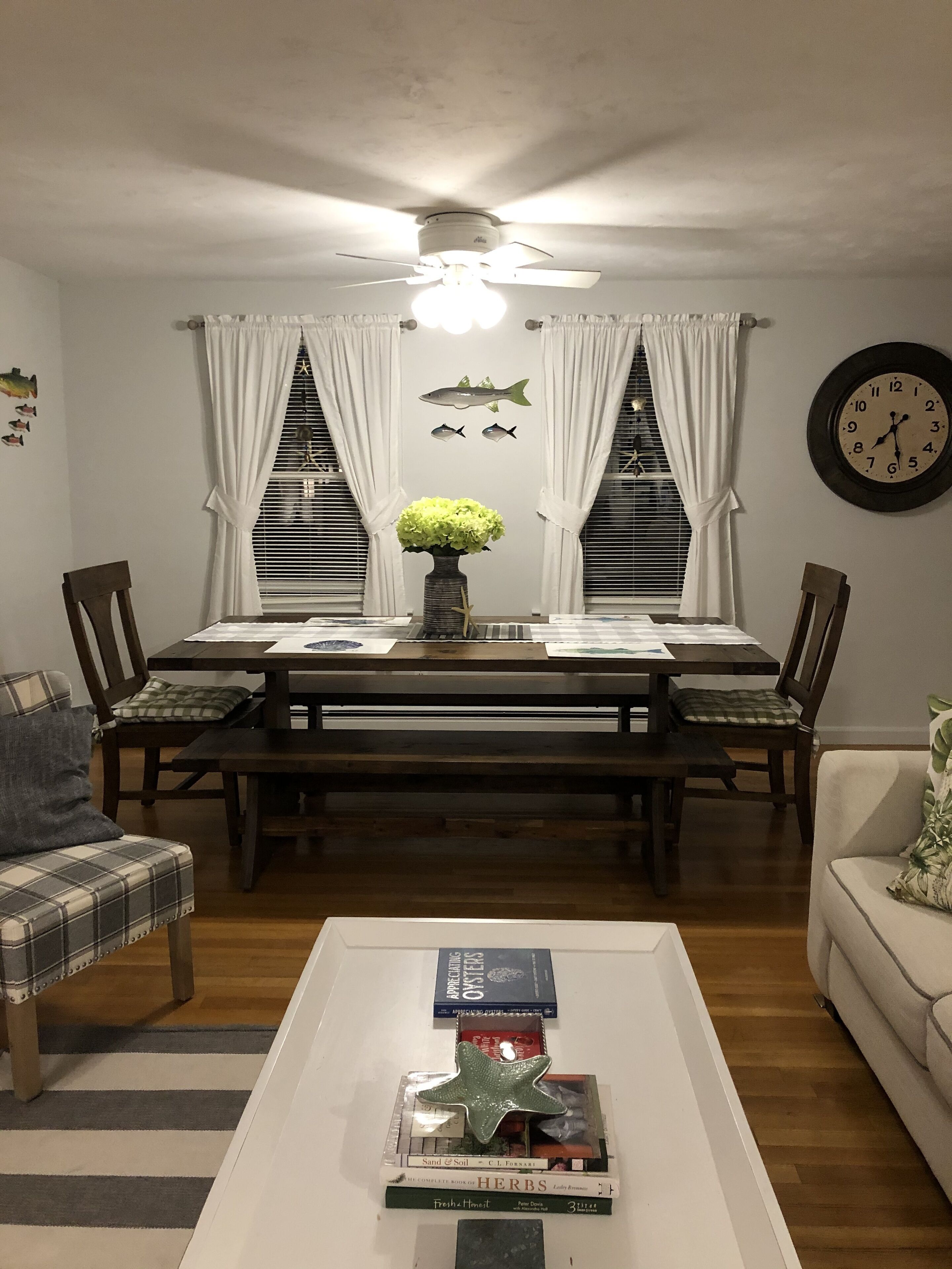 Un coin repas avec une table en bois, des chaises, un ventilateur de plafond et une horloge au mur.