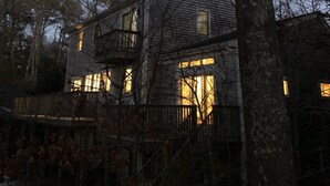 A two-story house with a balcony, surrounded by trees, under a night sky with a visible moon. - Stunning 4-bedroom Private Fresh Water Beach Front (East Falmouth)