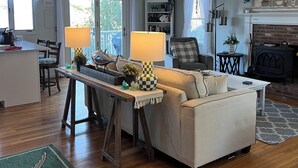 A living room with a sofa, a coffee table, a fireplace, and a bookshelf. - Stunning 4-bedroom Private Fresh Water Beach Front (East Falmouth)