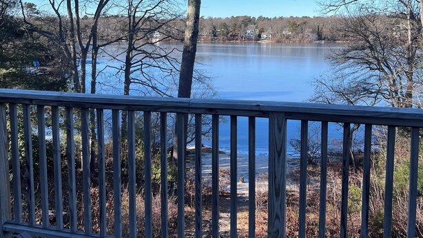 A wooden deck overlooking a calm lake with trees and houses in the background. - Stunning 4-bedroom Private Fresh Water Beach Front (East Falmouth)