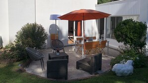 Une terrasse avec des meubles d’extérieur, notamment des chaises et une table, placée sous un grand parasol.